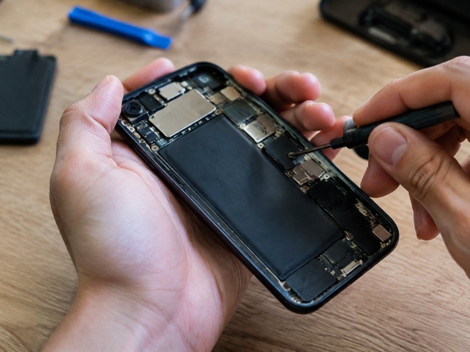 Mains tiennent un petit tournevis sur un smartphone ouvert